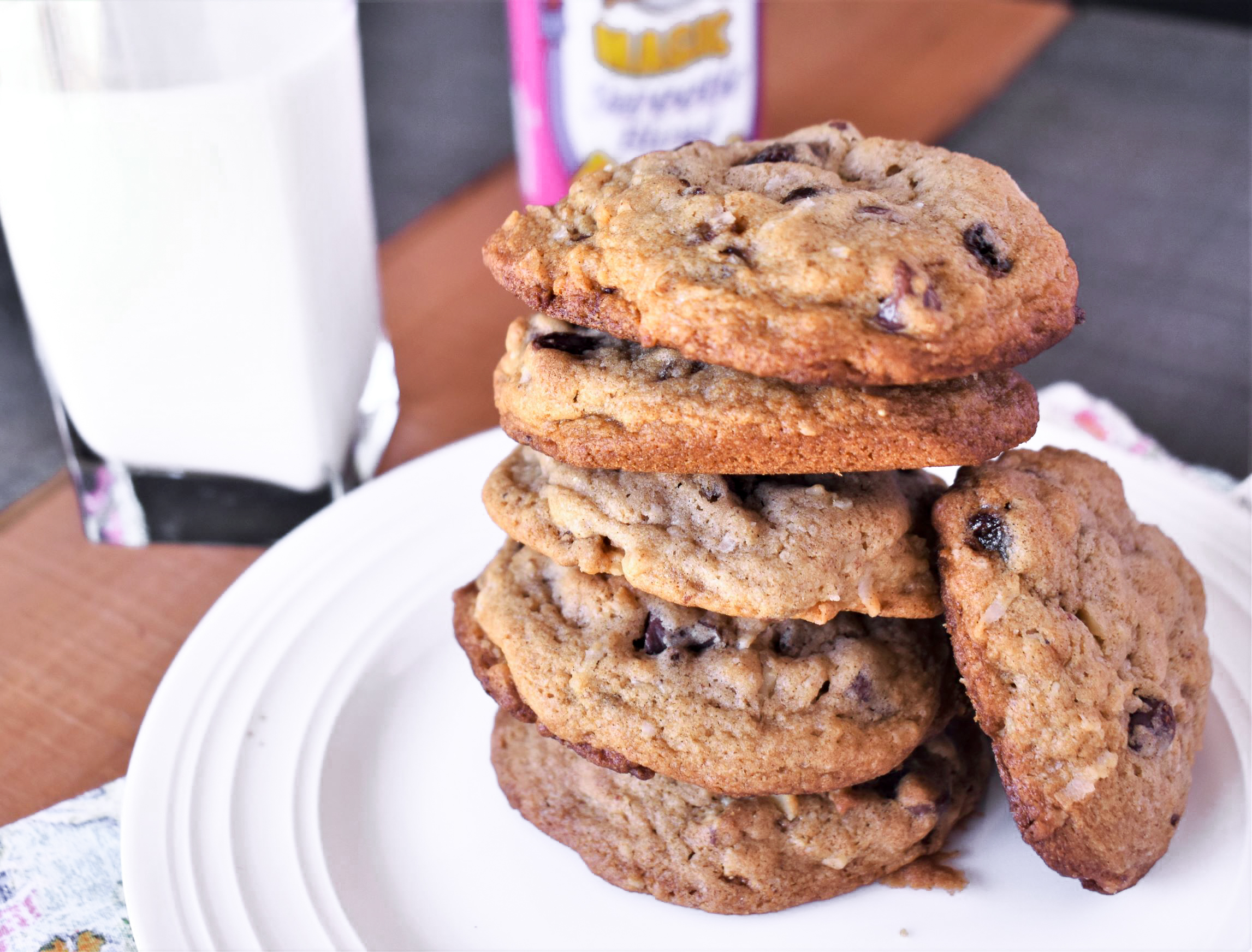 a plate of 6 lori's chocolate chippers stacked on eachother with one on its side, next to a glass of dairy milk